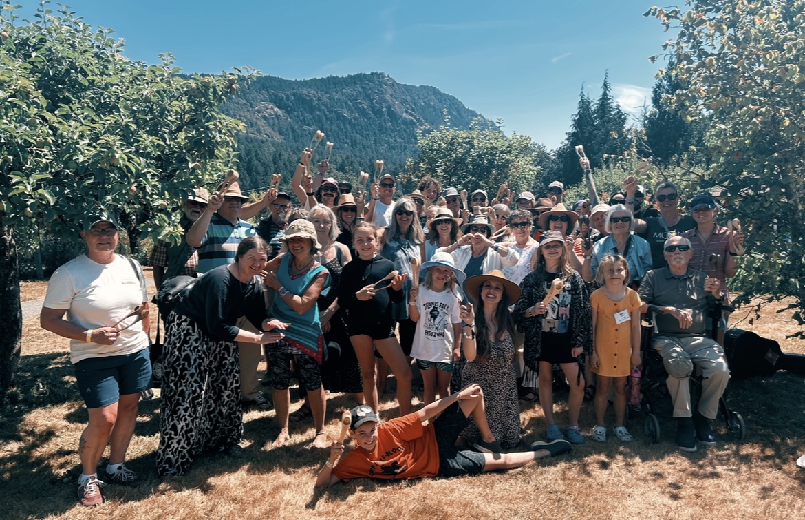 A spoon workshop group in the orchard holding up their wooden spoons